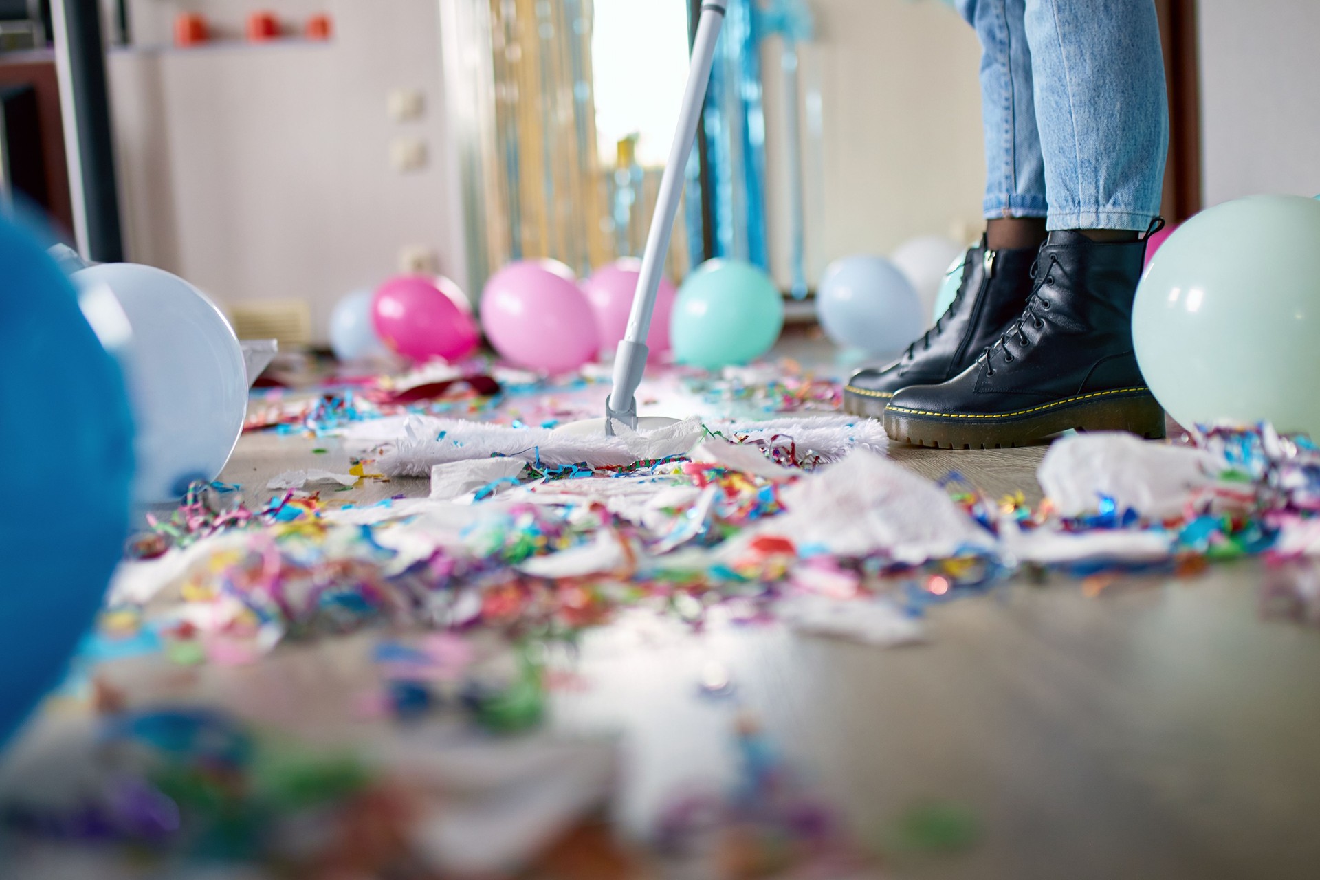 Woman with pushbroom cleaning mess of floor in room after party confetti